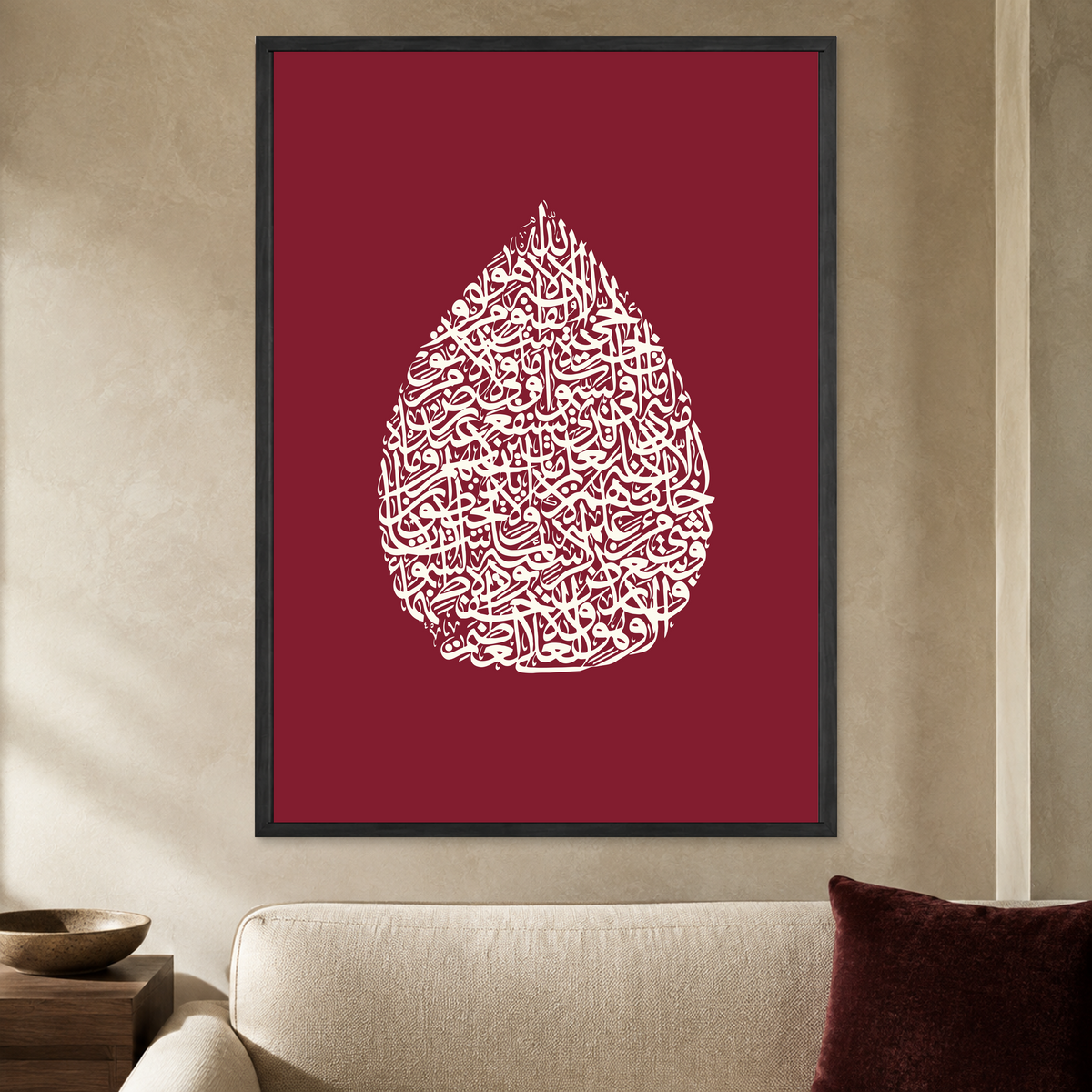 Cream teardrop-shaped Ayatul Kursi calligraphy on a burgundy wall poster in a black frame, styled in a living room
