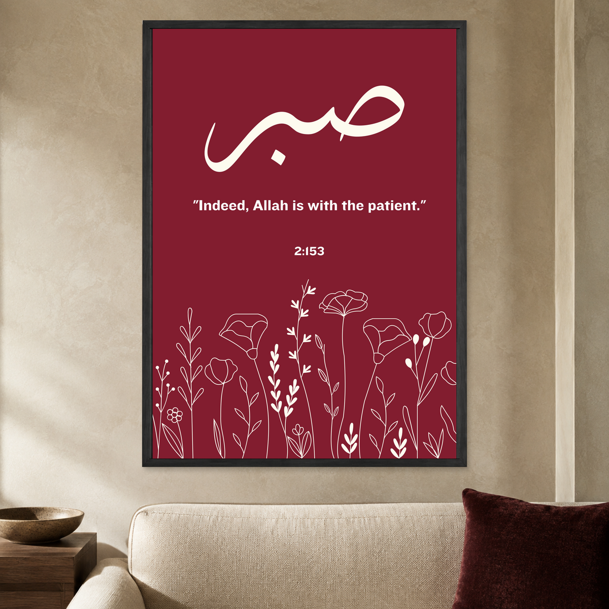 Burgundy Sabr wall poster with cream Arabic lettering, patience quotation and floral line art in a black frame, styled in a living room